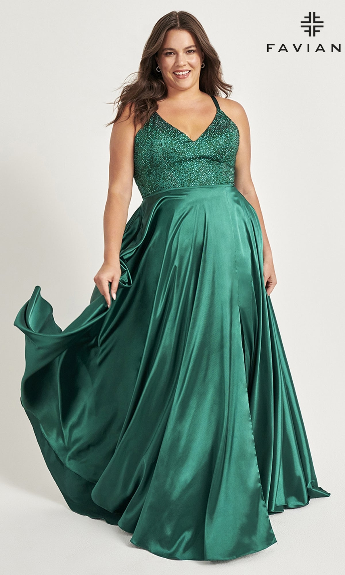 A woman in a Faviana Plus-Size Prom Dress with a strappy back, featuring an emerald green fitted sequin bodice and flowing satin skirt, stands against a plain background.
